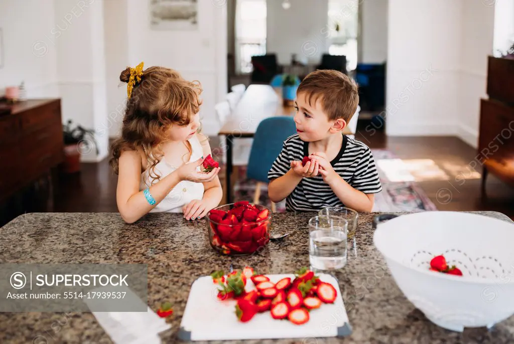 Brother and sister sharing fresh cut strawberries at kitchen island