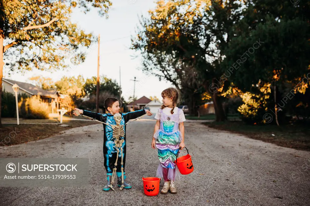 Young kids standing in street dressed up for halloween at sunset