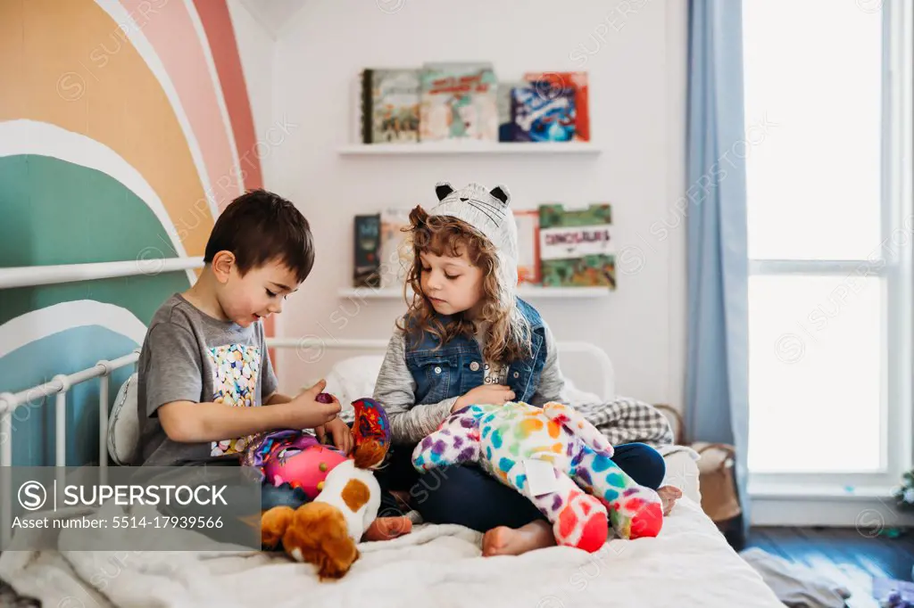 Brother and sister sitting on bed in rainbow kids room playing