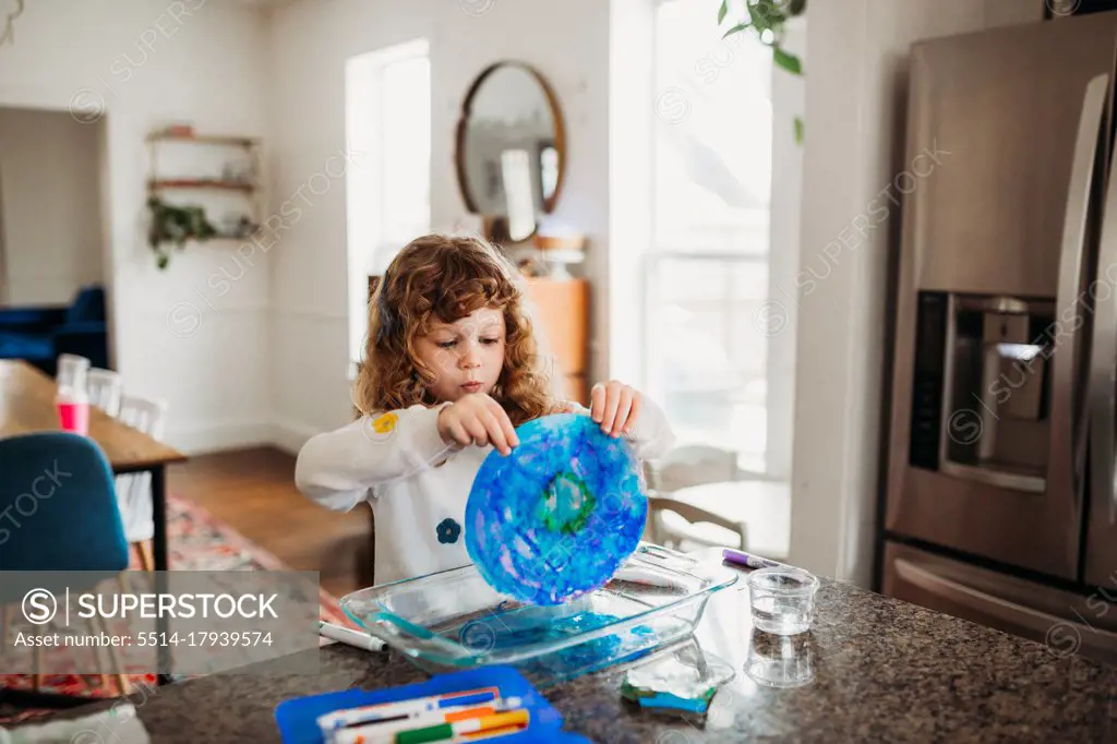 Young girl holding colorful art sitting at kitchen island