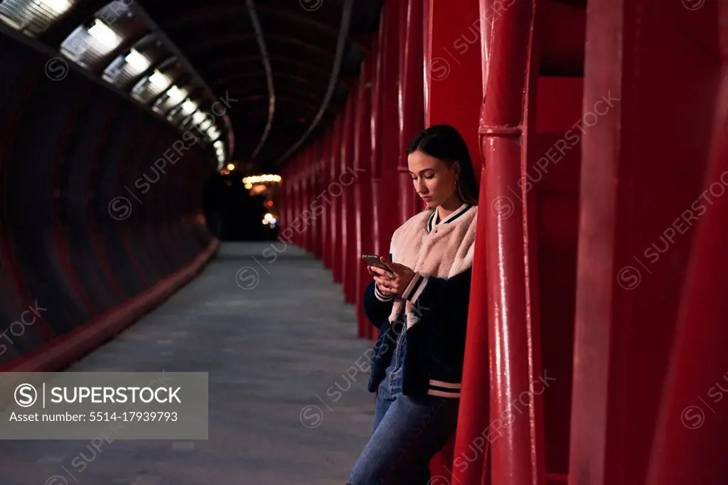Young woman looks at her mobile phone on a red bridge. Urban scene