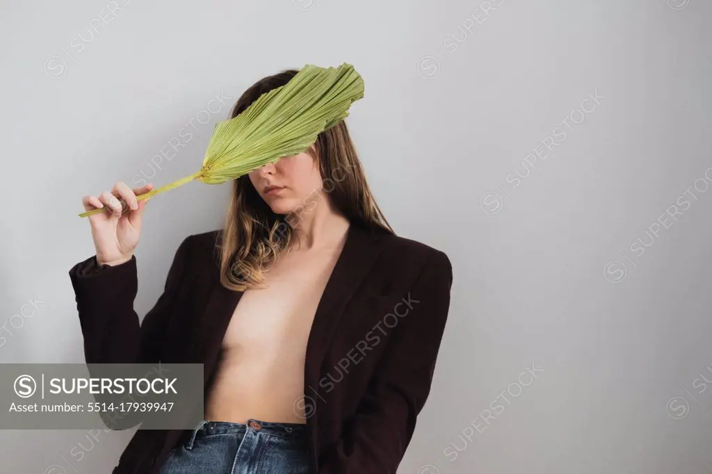 Woman in jacket above nacked body covers eyes with a palm leaf