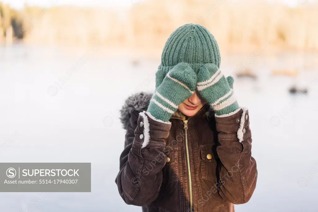 winter portrait of boy with wooly hat hiding behind his mittens