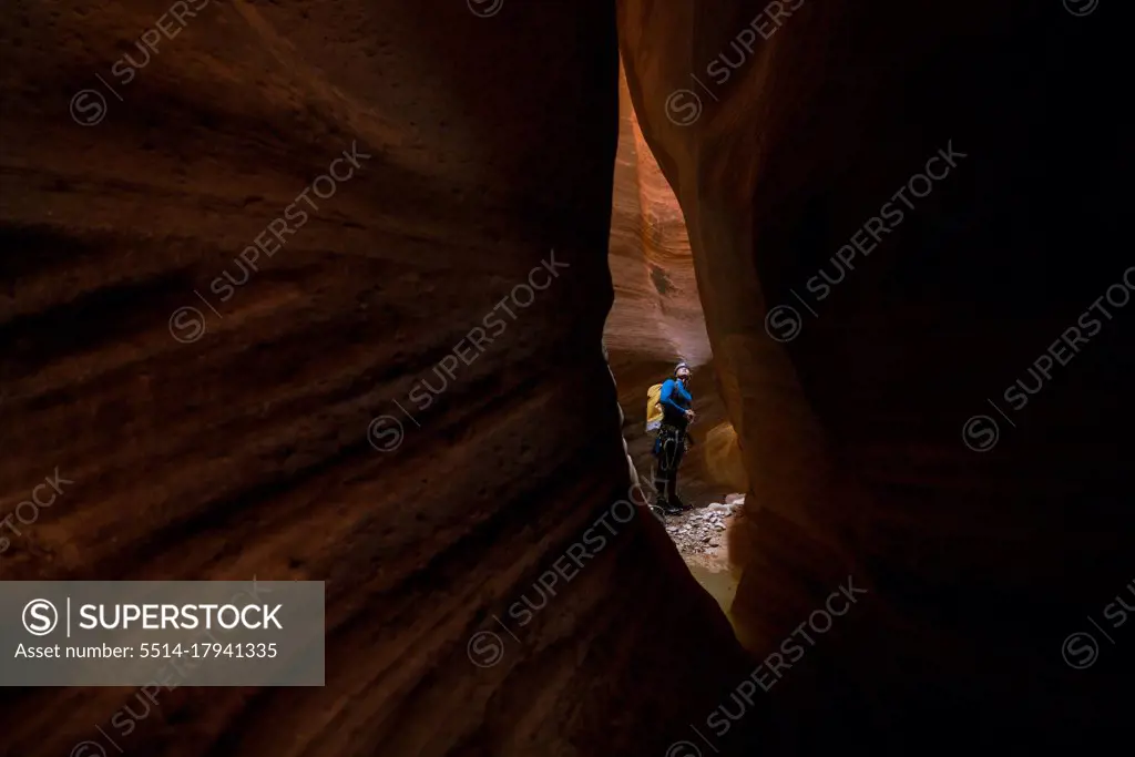 A man is seen through a small slit of red rock inside a canyon