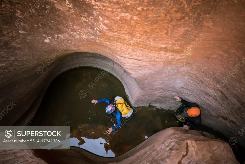 Two men wade through chest deep water to navigate a slot canyon