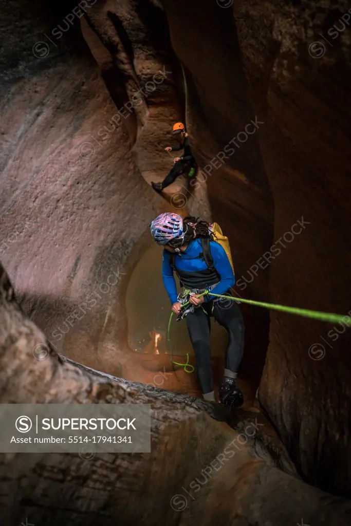A man rappels into slot canyon while his friend waits in the distance
