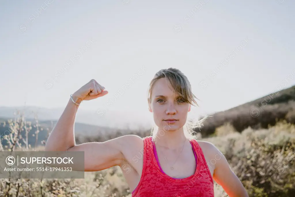 Athletic blonde woman flexes muscles with sun and mountains behind