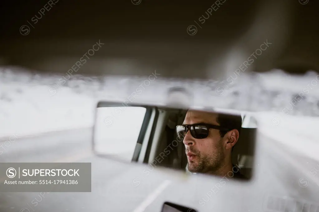 A man is seen whistling to music in the rear view mirror of his van