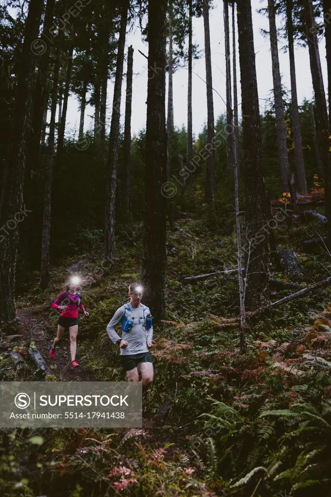 Two trail runners run down steep slope at night with headlamps glowing