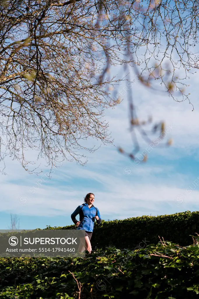 Young woman run on paved trail under trees and blue skies