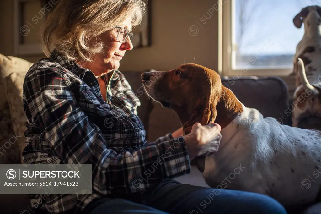Happy Senior Citizen plays with dogs ears sitting on couch at home