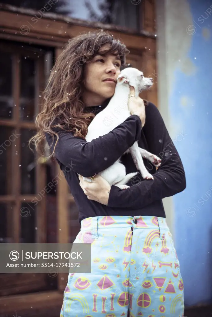 Woman with snow in hair holds small white dog to stay warm outside