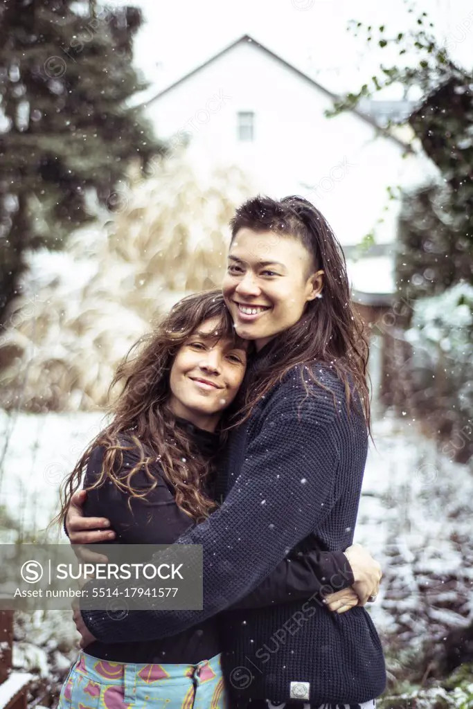 mixed-race queer women couple hug and smile in snow in europe winter