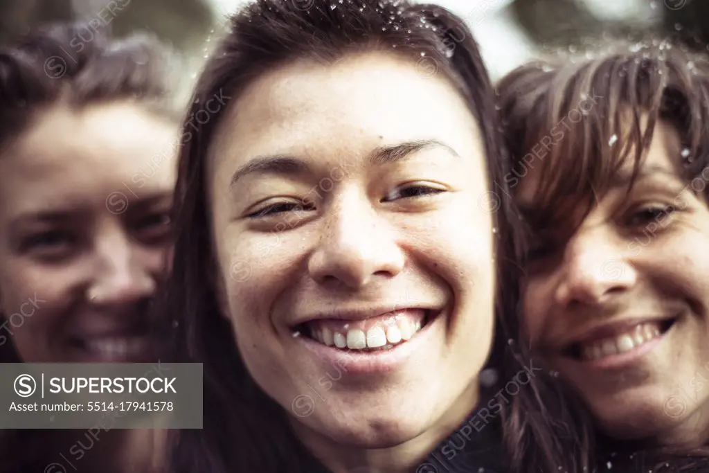 three women fill frame with happy smiles and snow in hair in winter