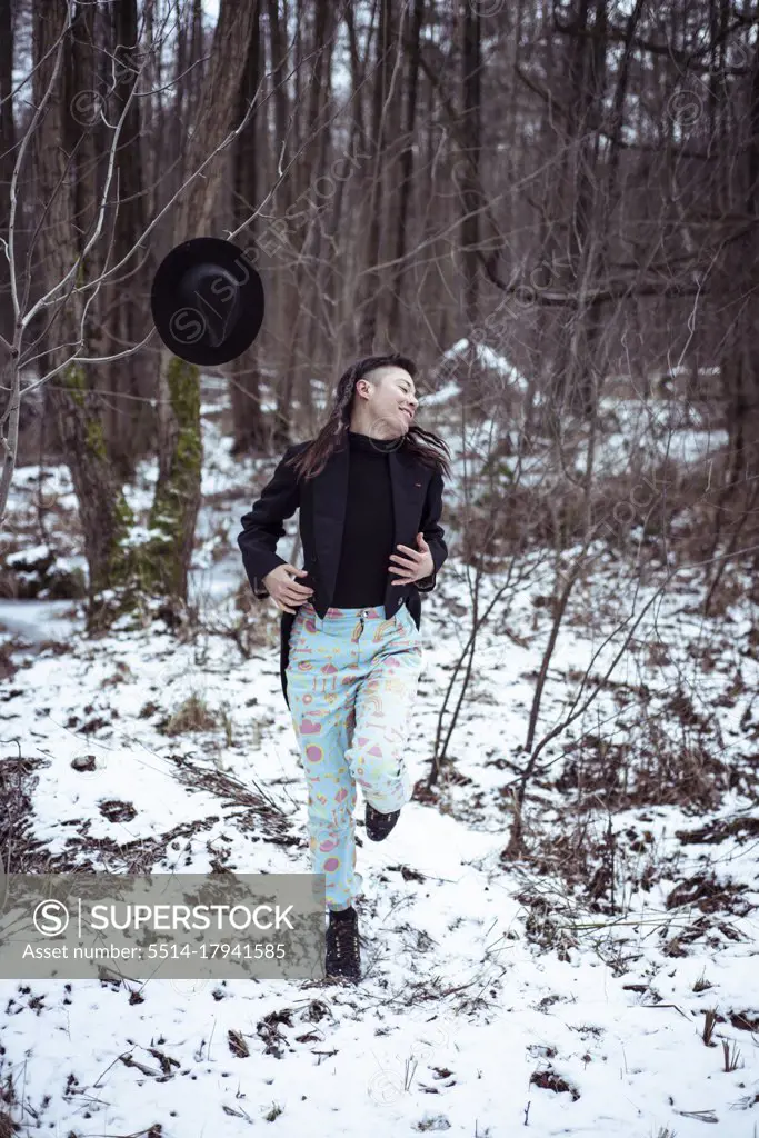 Playful dancer laughs and moves in snow covered forrest with tuxedo