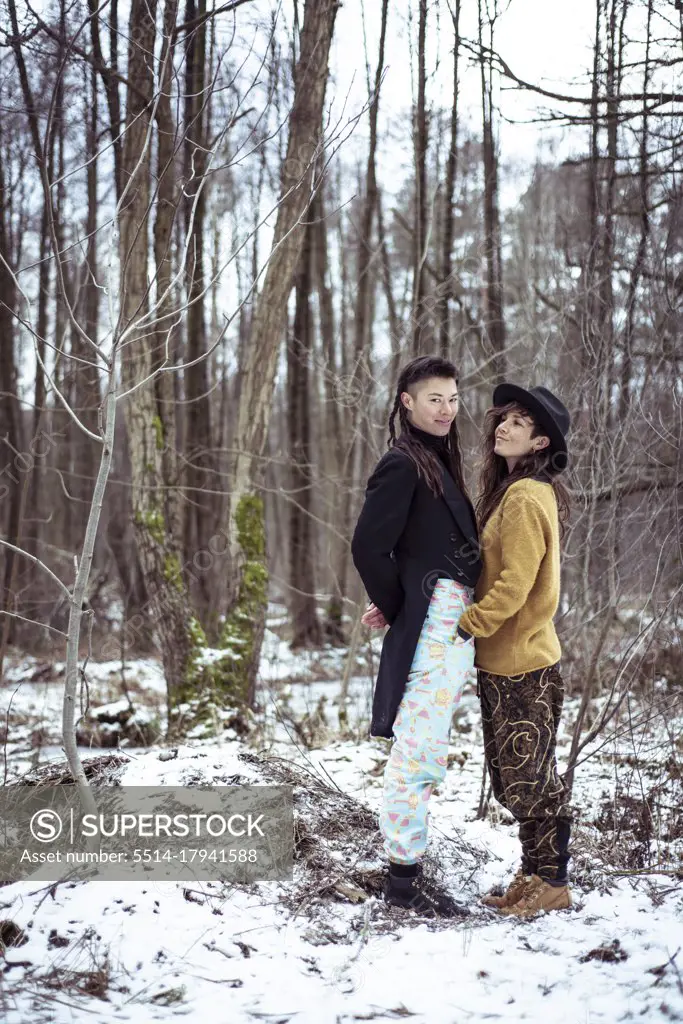 queer female couple smile together in the snow covered forrest