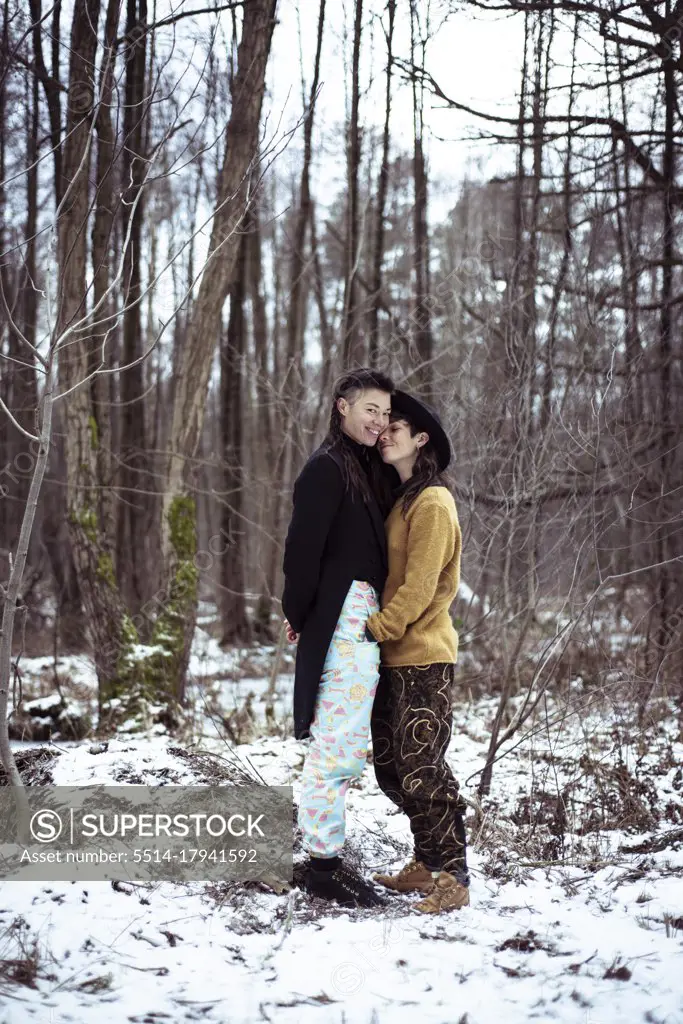 queer lesbian couple smile and cuddle in snow covered woods in germany