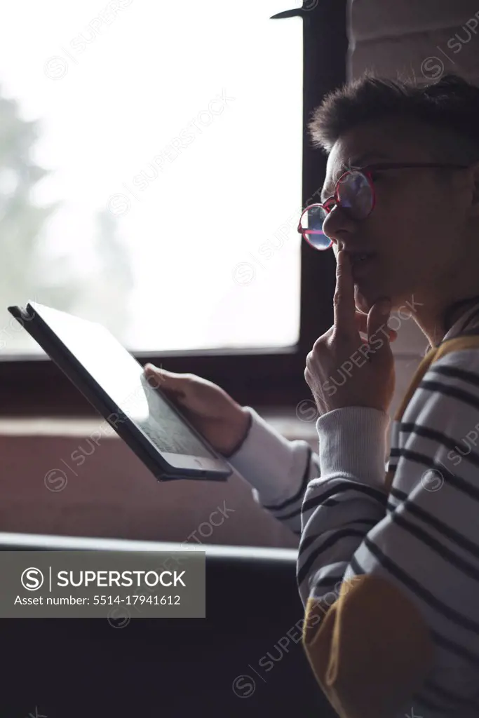 queer asian woman with glasses sits thoughtfully with ipad device