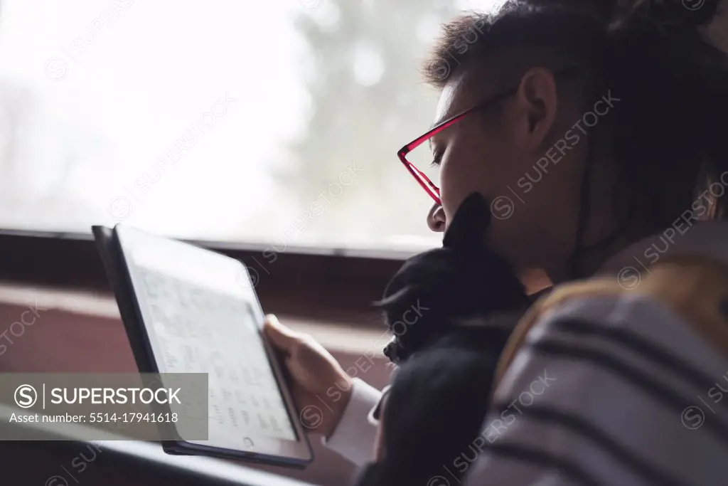 woman in glasses lit by window with small puppy reading spreadsheet