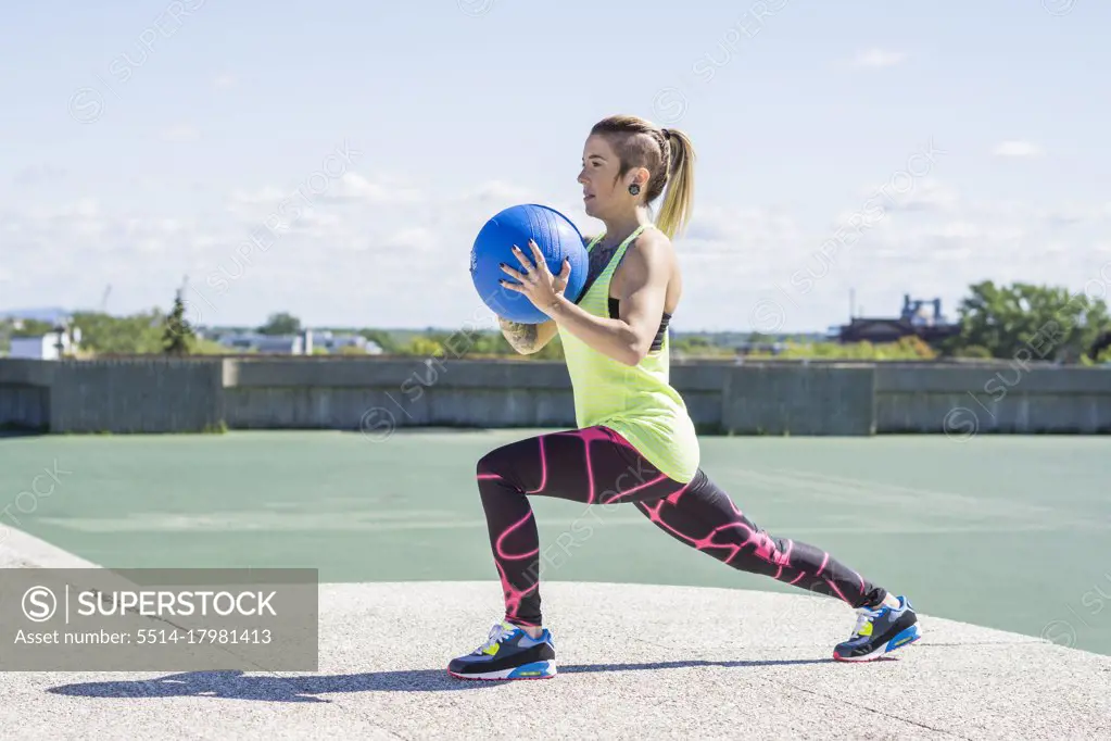 Female athlete working out with medicine ball on summer day