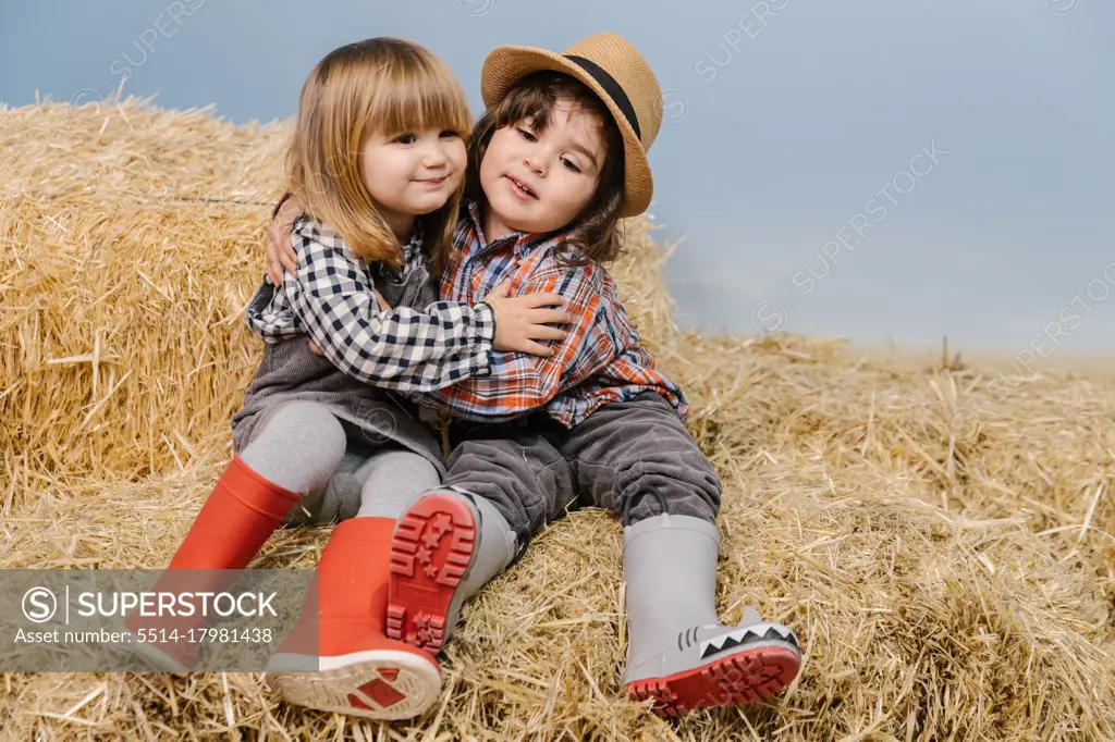 Two little kids embracing each others while sitting on straw bales. Ag