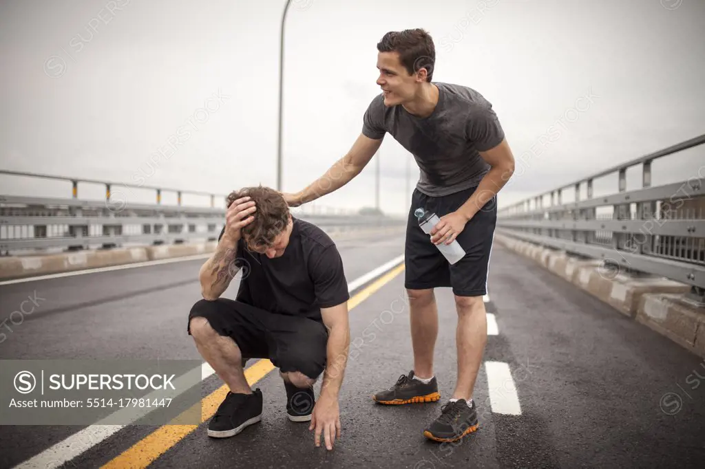 Supportive male athlete helping friend trying to rehydrate durin