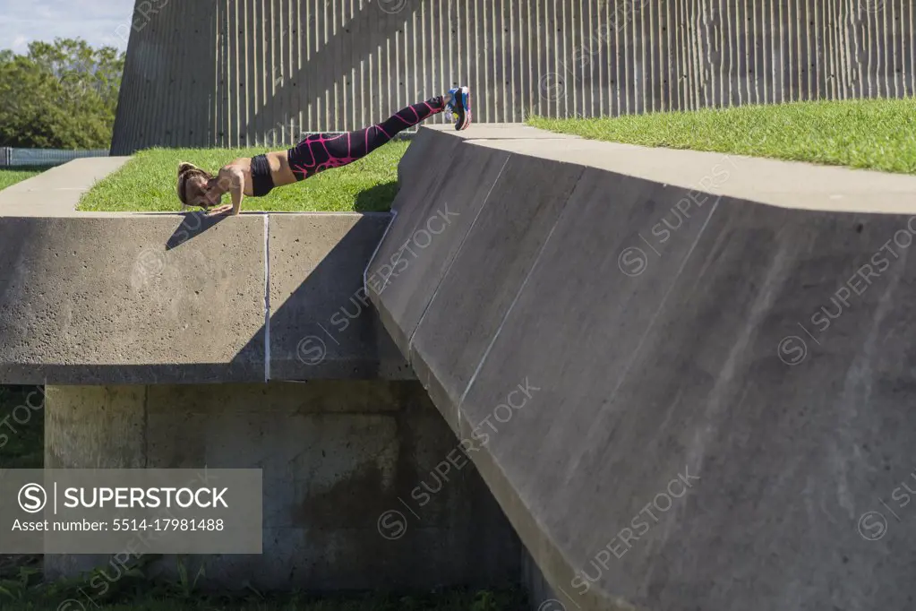Female athlete doing elevated push ups on summer day in concrete