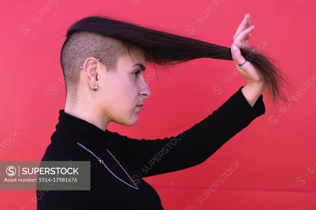Young hipster woman in profile and stretches her hair in front of a red wall
