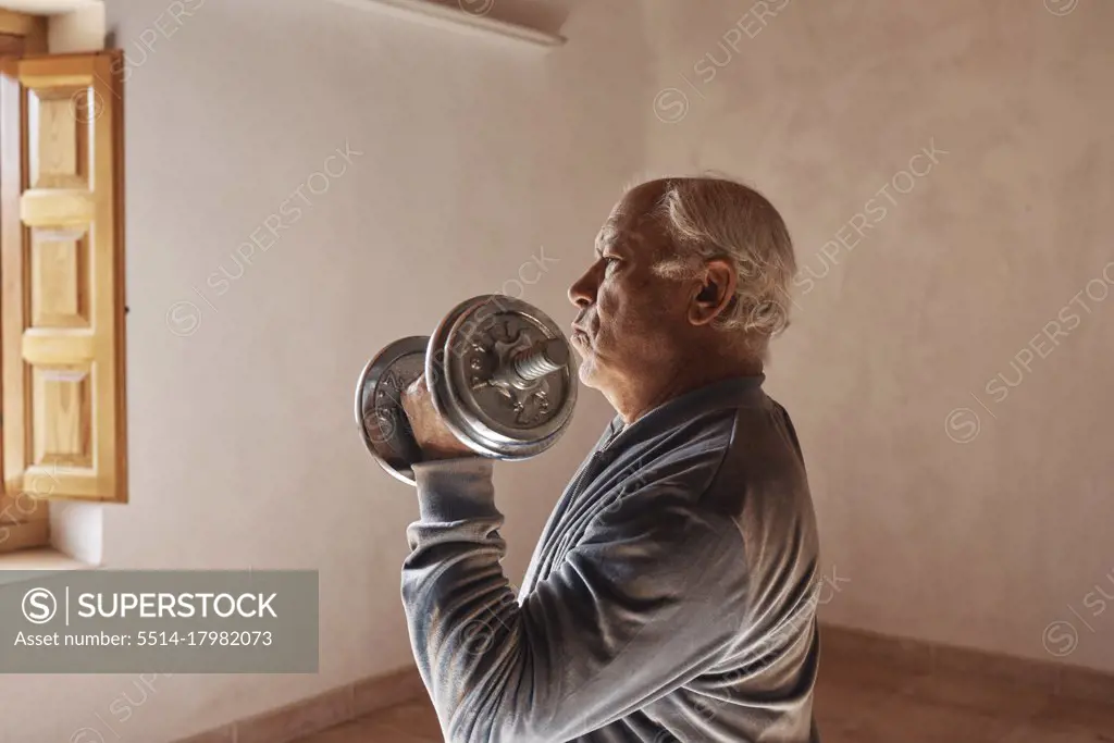 Old man with white hair lifts weights at home
