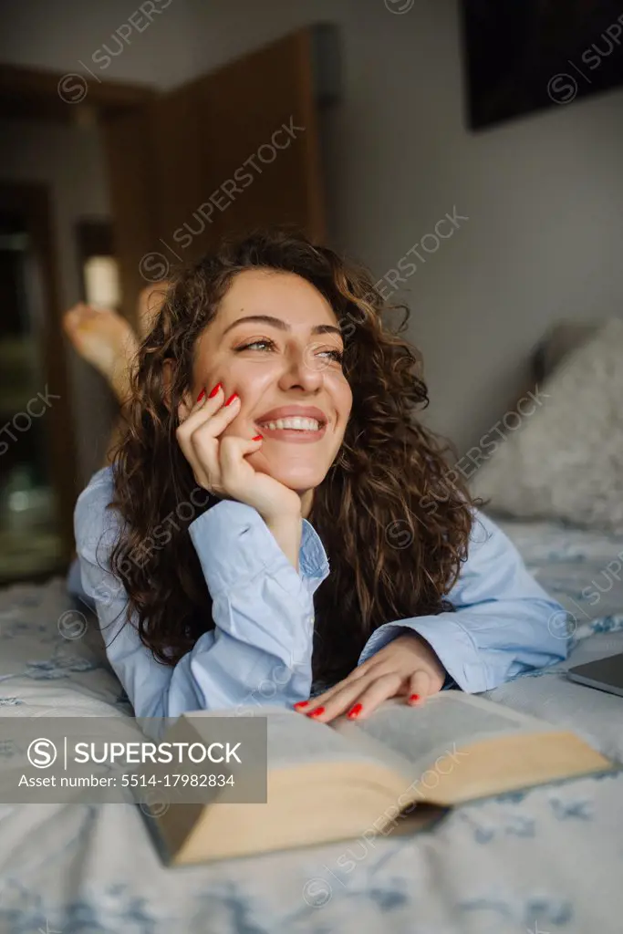 Happy young woman readding a book lying in bed.