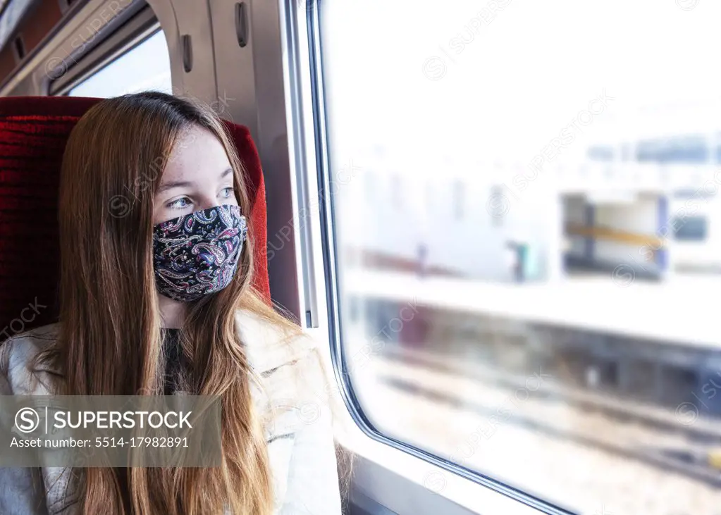 Young teenager looking concerned travelling on a train wearing a mask