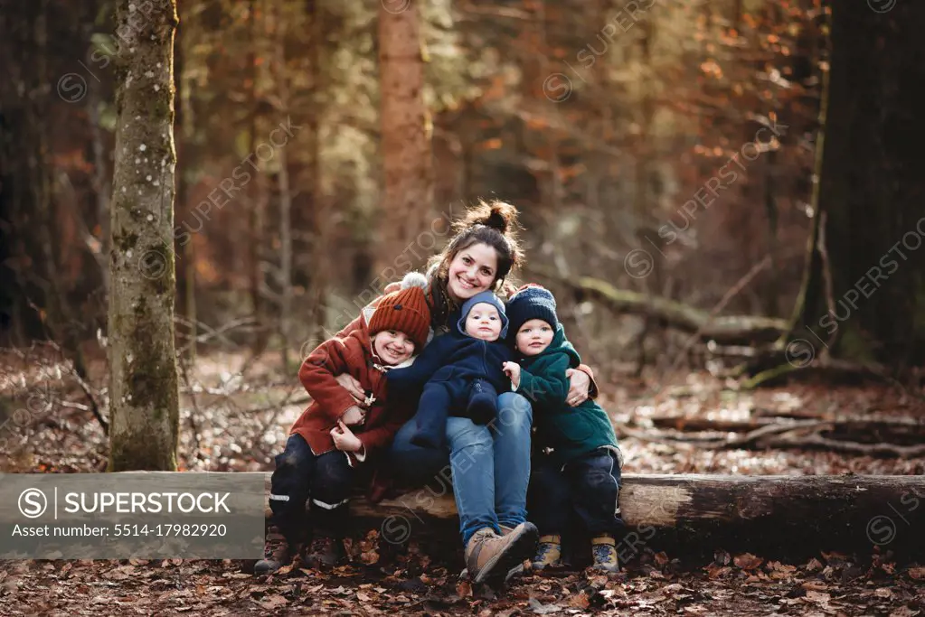 Mom and children smiling happily sitting in forest in the Fall