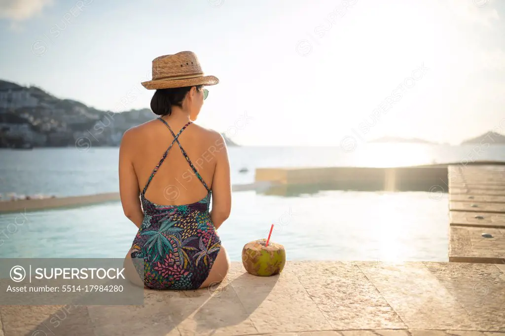 Happy woman relaxing in the swimming pool and drinking coconut water.