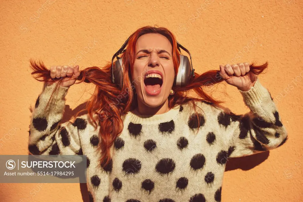 White Caucasian woman with red hair wearing helmets to protect herself from noise pulls her pigtails while screaming. Noise concept