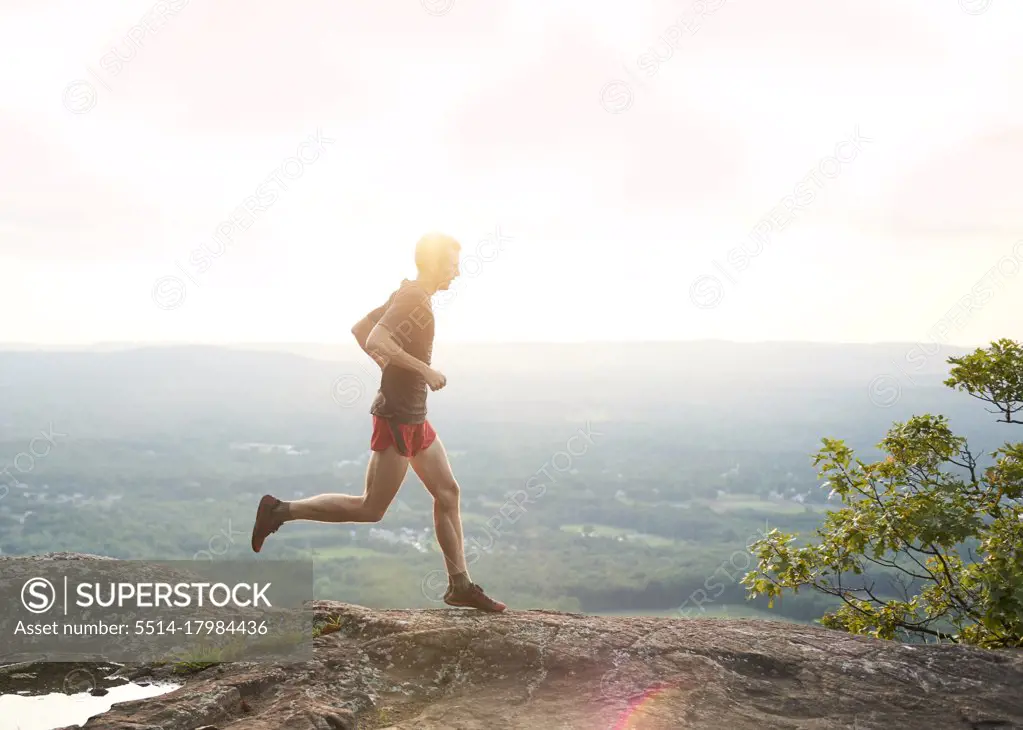 Adult male trail runner on a mountain ridge at sunset
