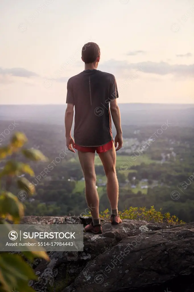 Adult male trail runner climbing on a mountain ridge at sunset