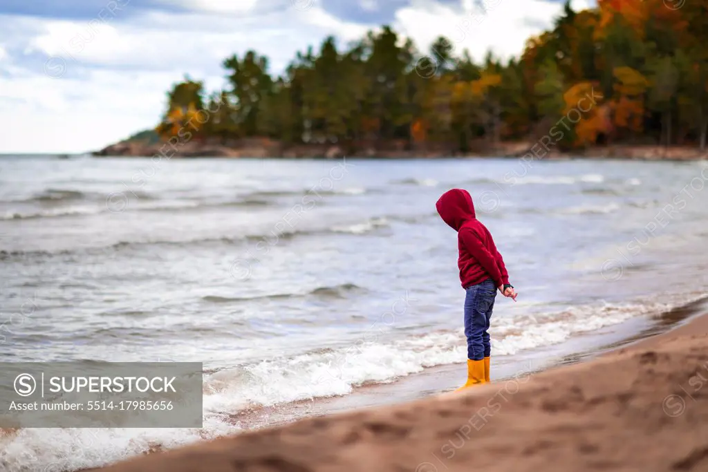 boy standing on shore line of Lake Superior looking down at water