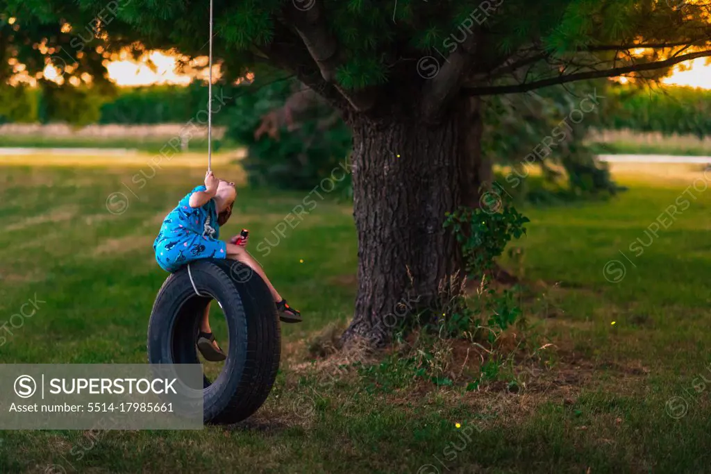 boy in pajamas on tire swing with flash light collecting fire flies