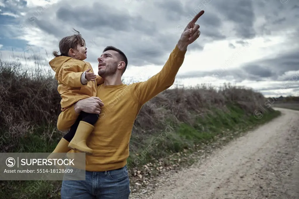 A dad pointing out something to his 2 year old daughter in natur
