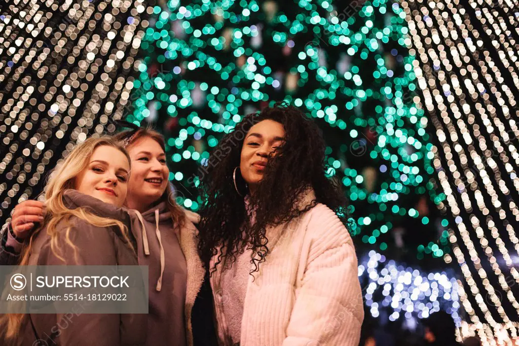 Happy female friends standing by Christmas tree in city at night