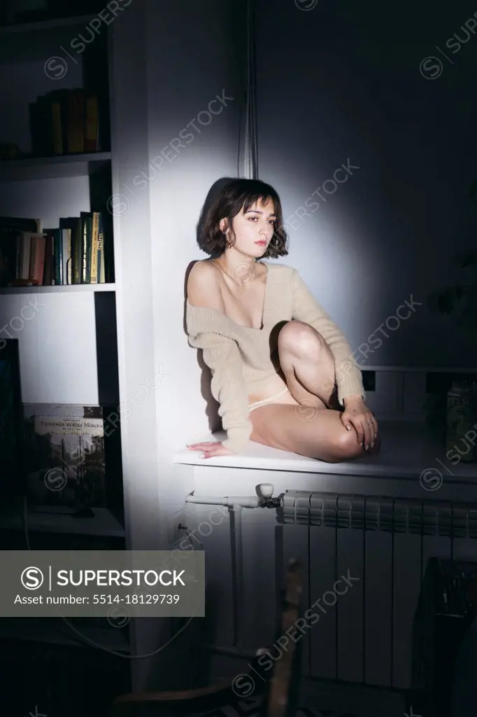 a woman sits on the windowsill in the evening in panties