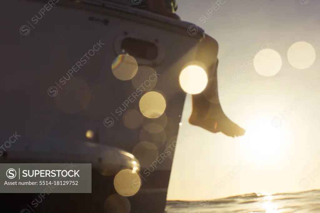 feet hanging over boat at sunset