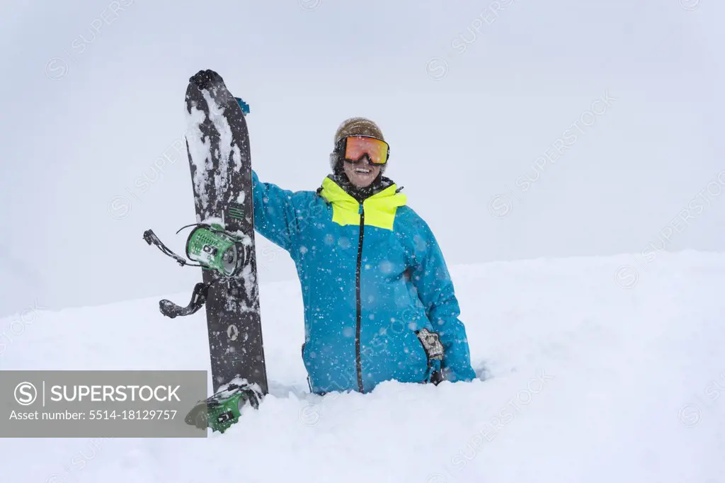 young male standing with snowboard in deep snow in the mountains