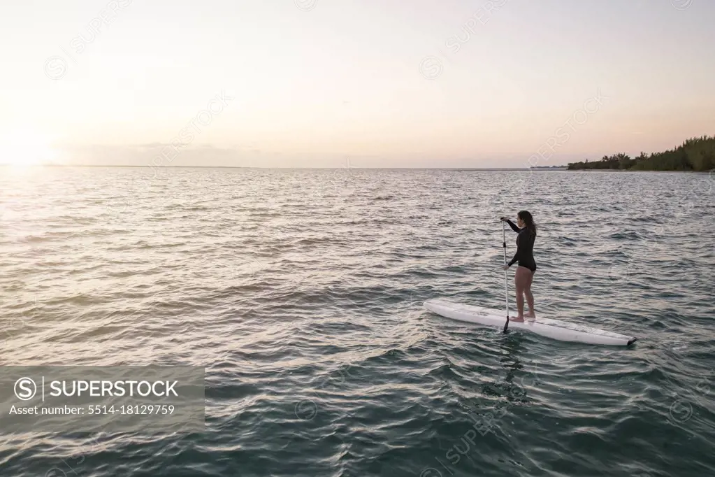 young asian female paddleboarding in Bahamas at sunset