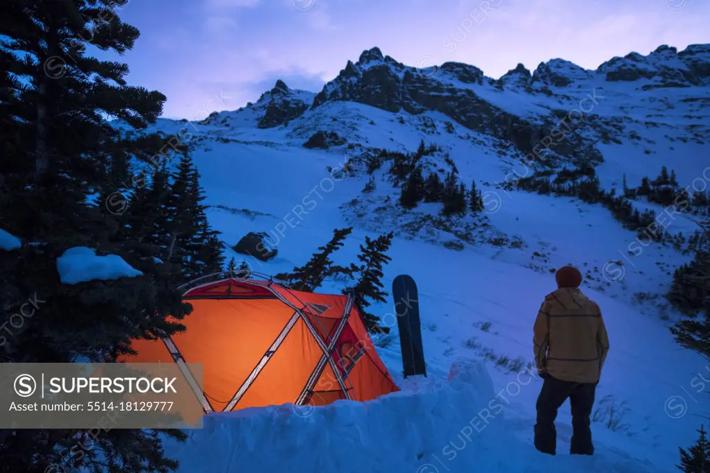 Young male standing outside tent at twilight in winter