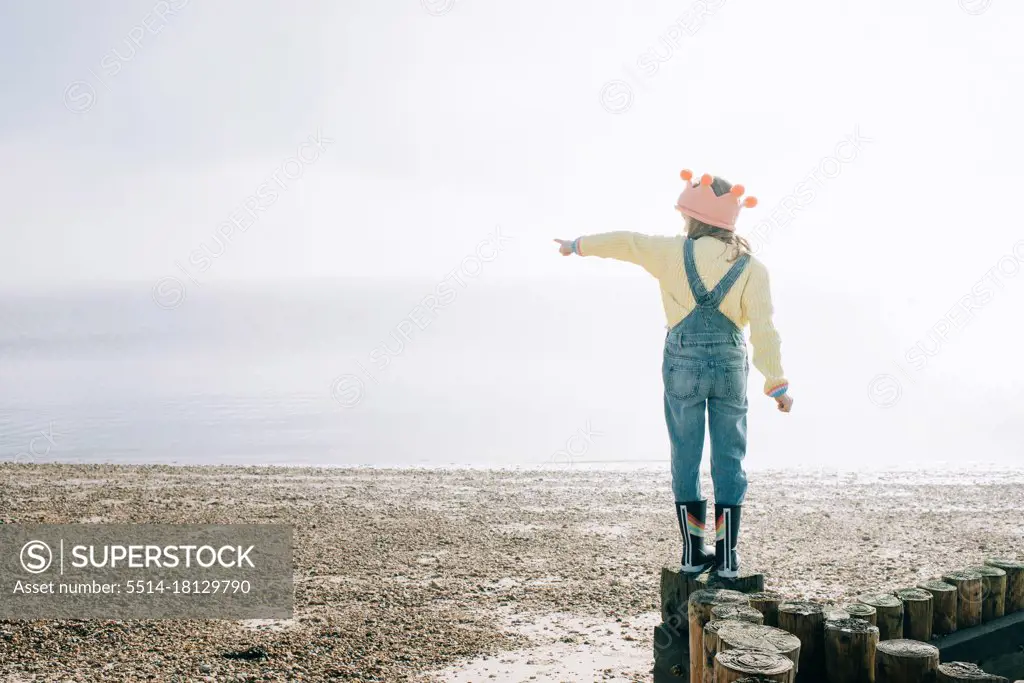 young girl stood at the beach pointing to the ocean on a sunny day