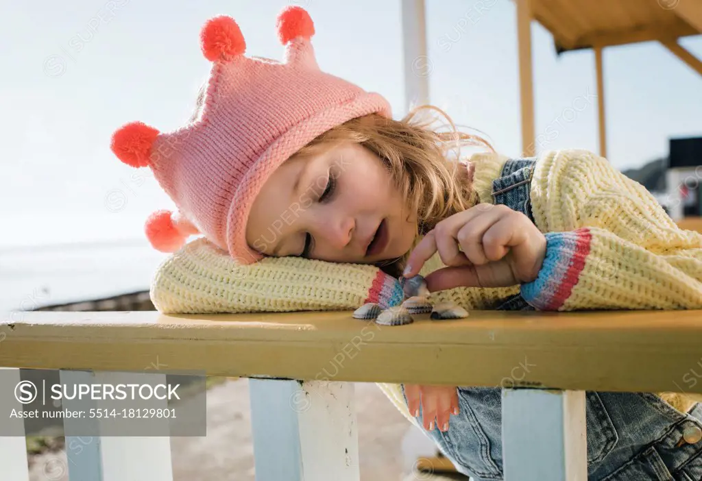 child playfully choosing shells using her imagination at the beach