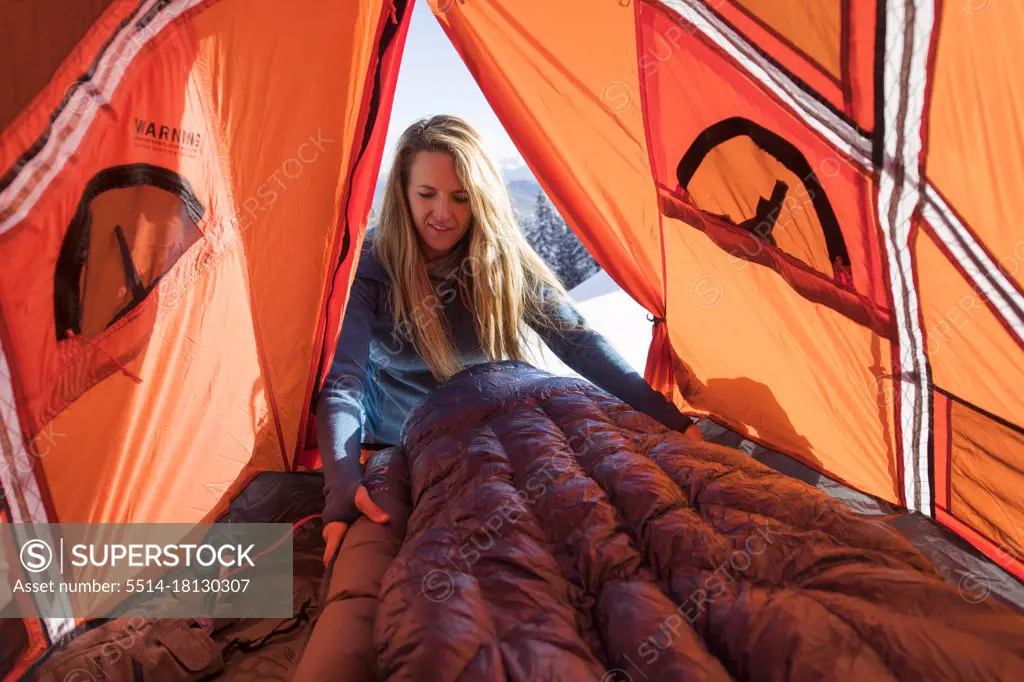 Young female setting up sleeping bag in tent while winter camping