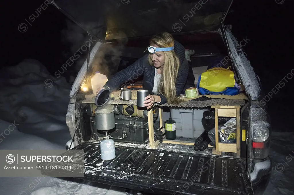 Young female making tea in back of truck while winter camping