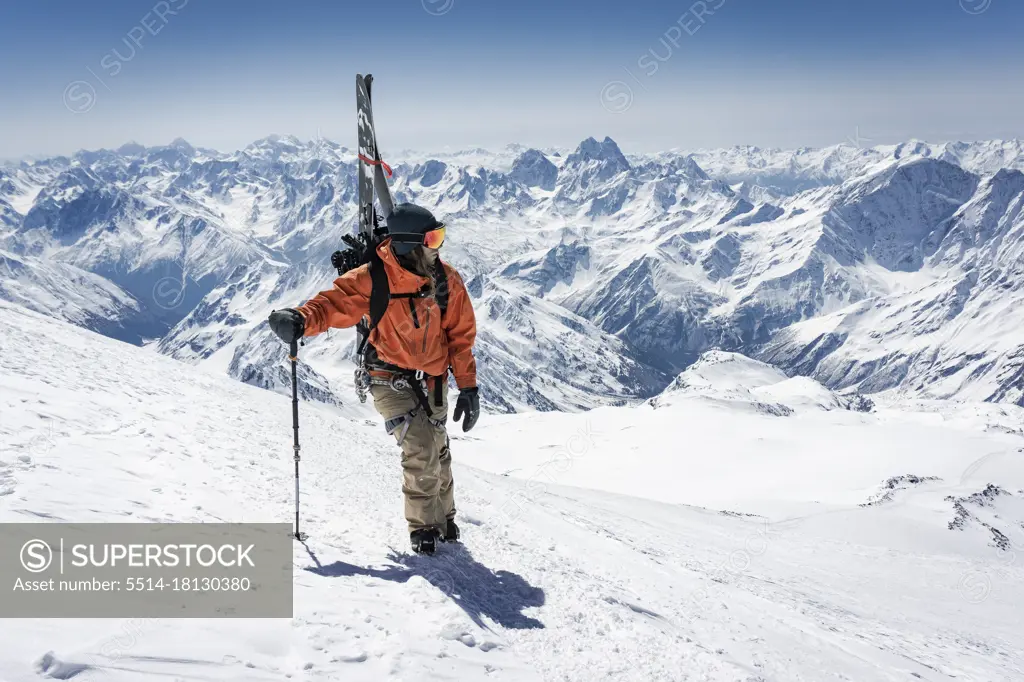 Man with ski pole carrying splitboard while climbing snowcapped mountain during vacation